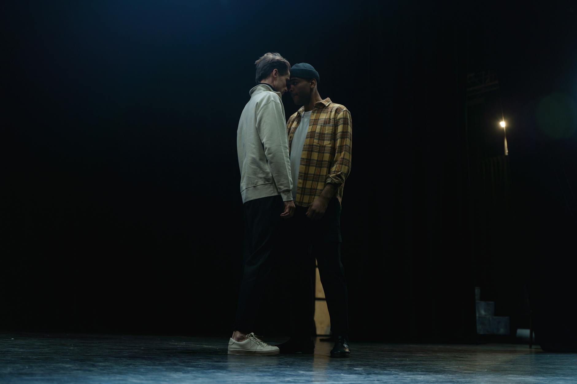 Dwóch aktorów ćwiczy emocjonalną scenę na przyciemnionej szkolnej scenie