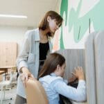 Nauczyciel wspiera ucznia przy komputerze w nowoczesnej jasnej klasie