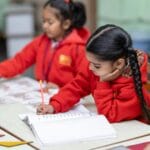 Uczniowie w czerwonych mundurkach piszą test przy szkolnych ławkach