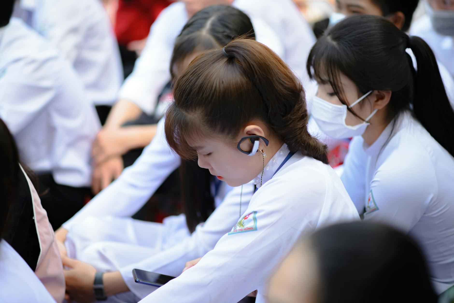 Uczniowie w szkolnych mundurkach korzystają z telefonów i słuchawek