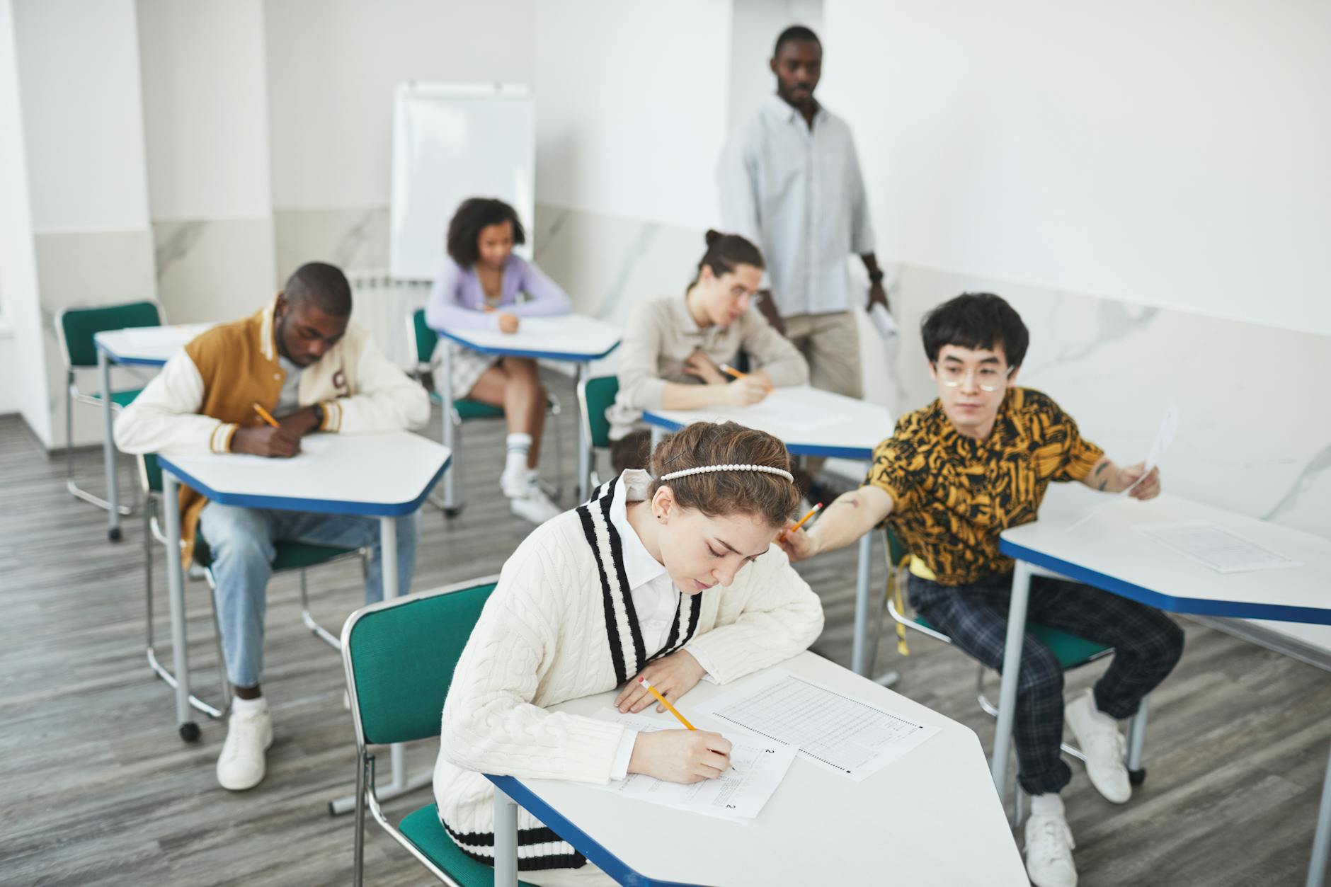 Uczniowie piszą test w nowoczesnej sali, nauczyciel nadzoruje pracę